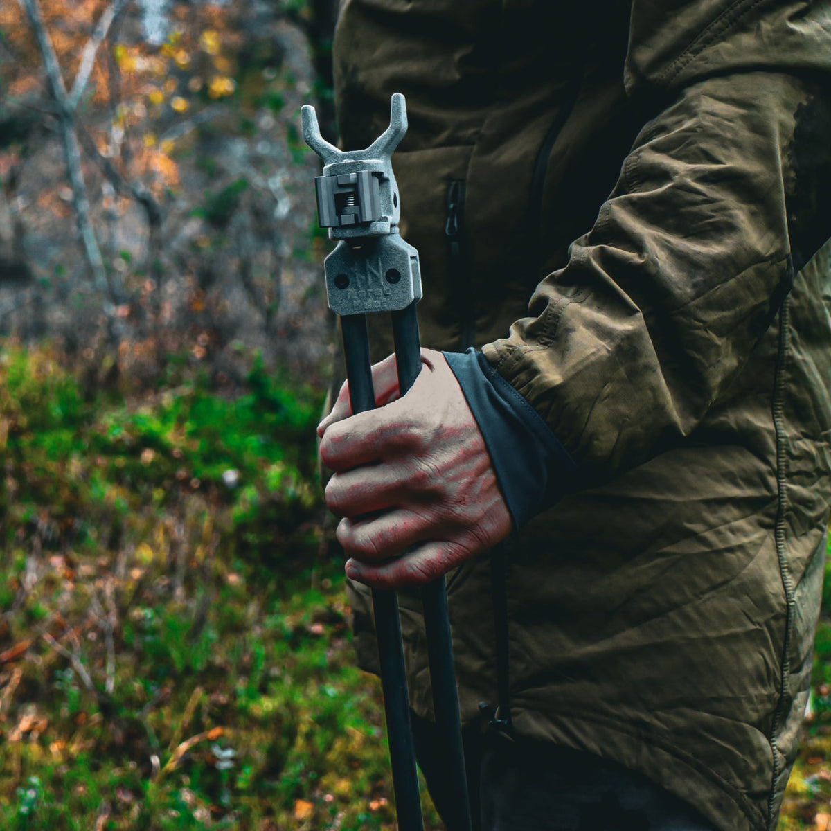Person holding folded NorneHunt shooting sticks upright with the V-cradle visible at the top.