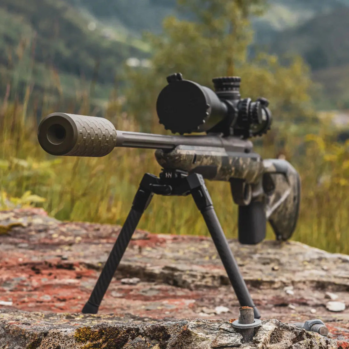 NorneHunt SvartR bipod supporting a scoped hunting rifle on a lichen-covered rock in autumn terrain.