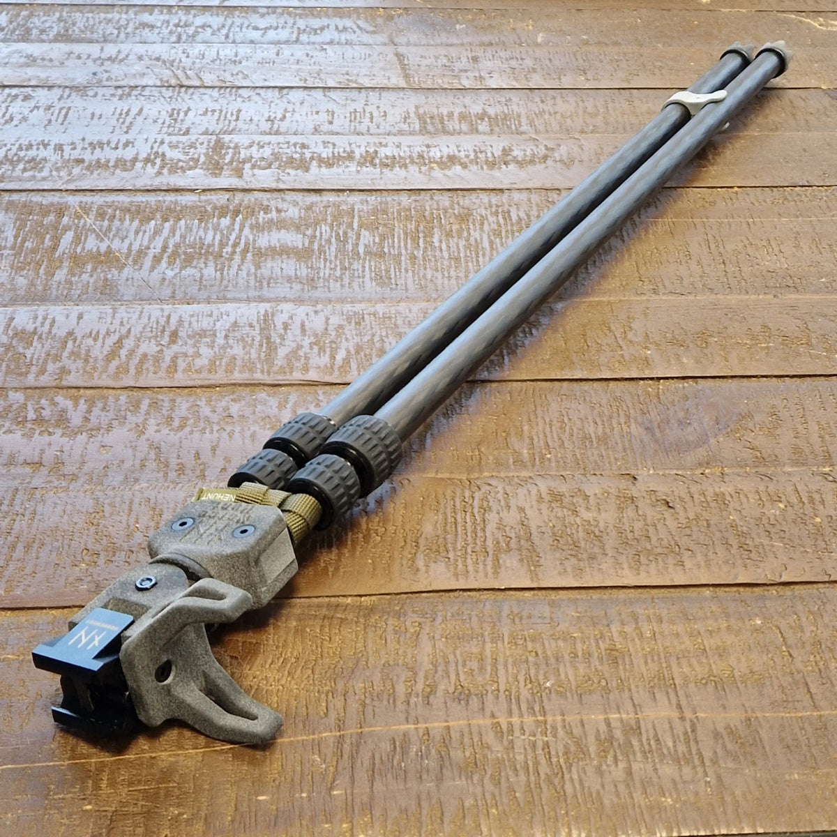 NorneHunt carbon fibre shooting sticks folded together on wooden boards, with the head and Picatinny clamp visible.