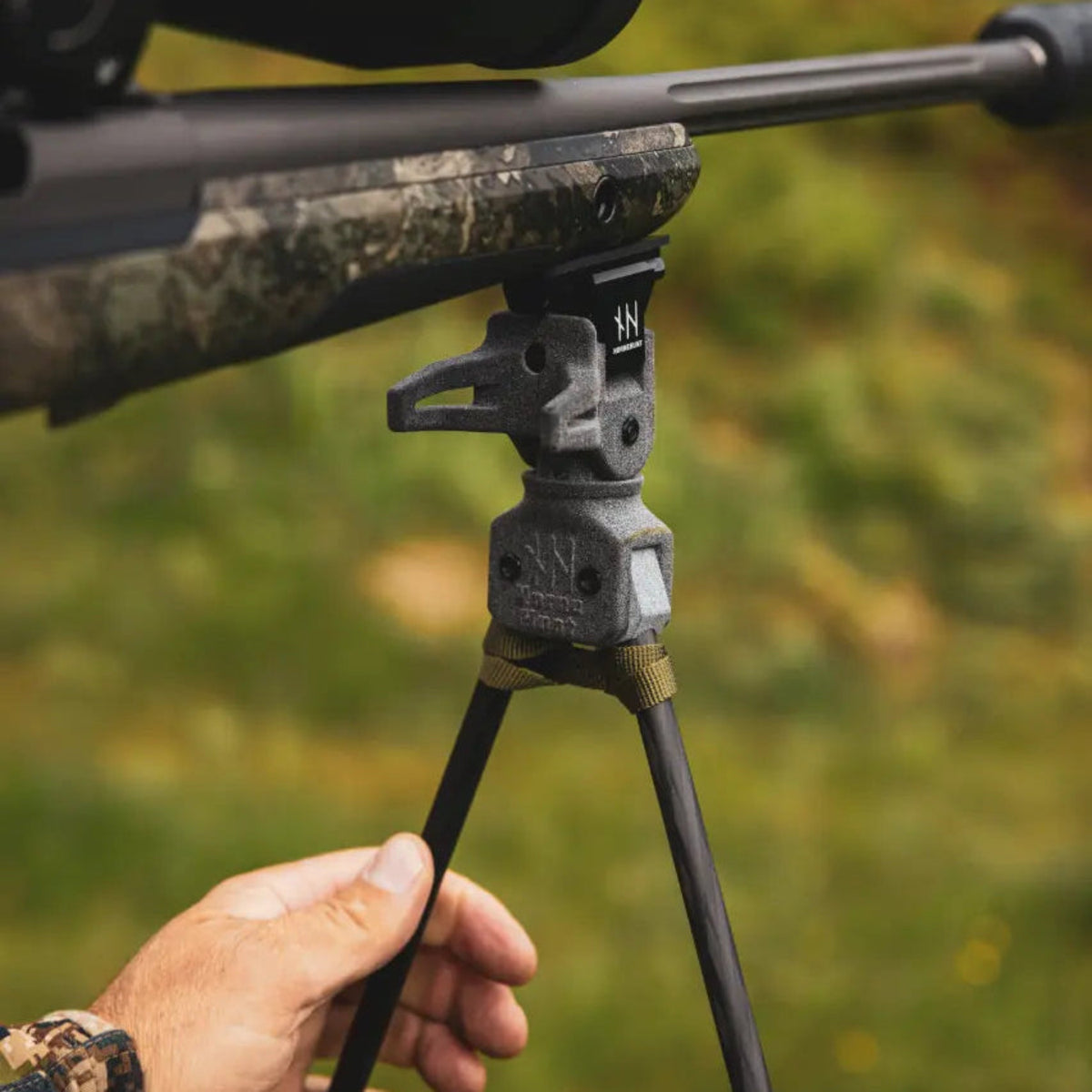 Close-up of NorneHunt shooting sticks attached to a rifle's Picatinny rail, with a hand holding one leg.